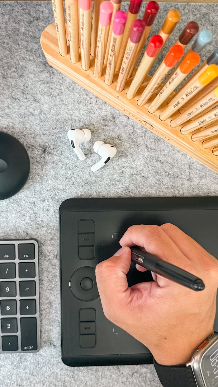 Overhead view of a digital drawing setup with stylus and colored pencils on a desk.